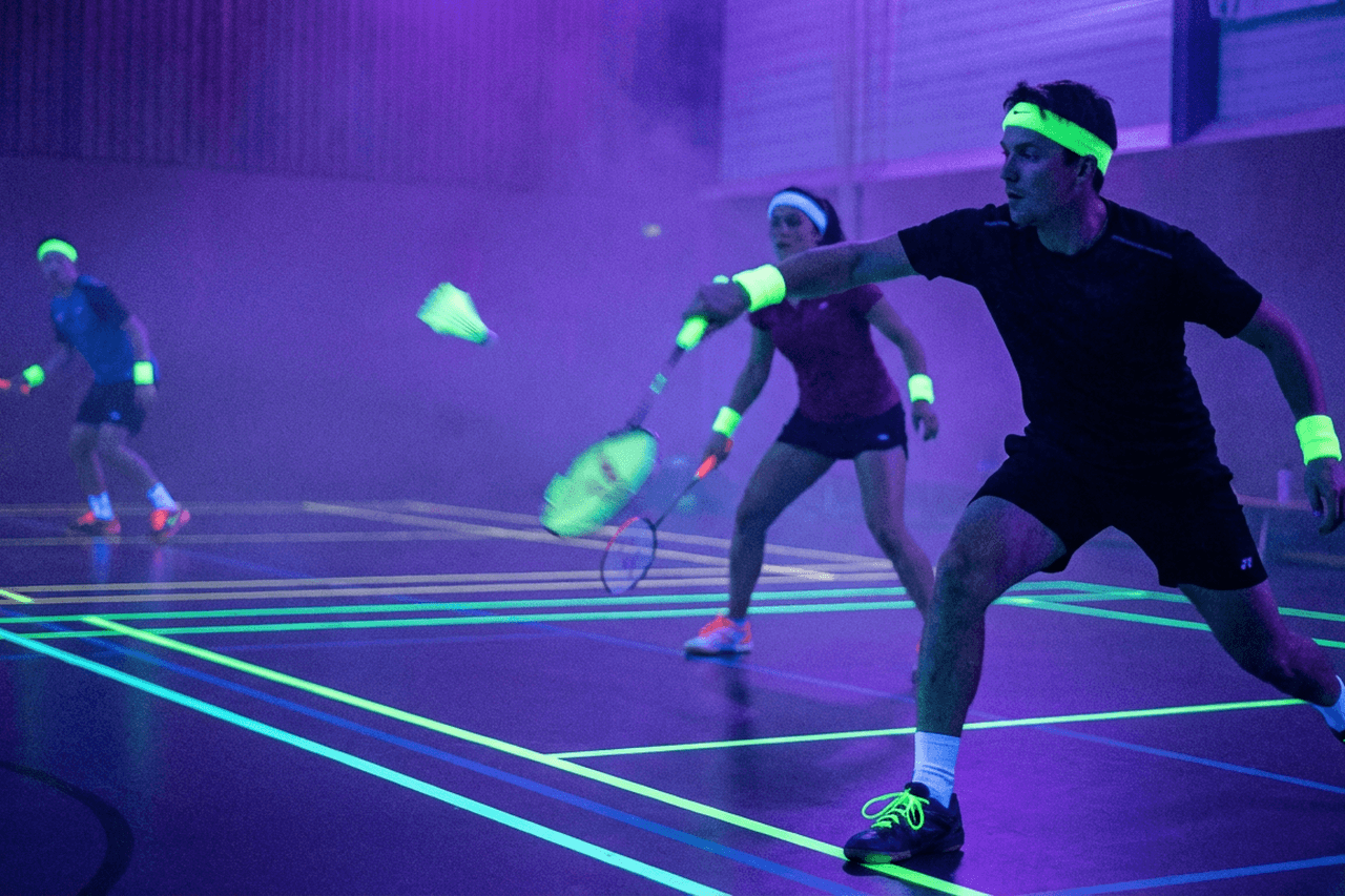Glow in the dark badminton in een sporthal met UV-verlichting en neonlijnen